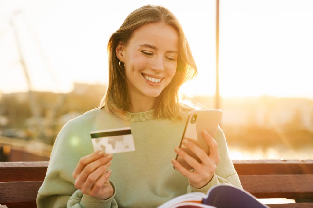 Portrait of smiling young woman holding cellphone and credit card